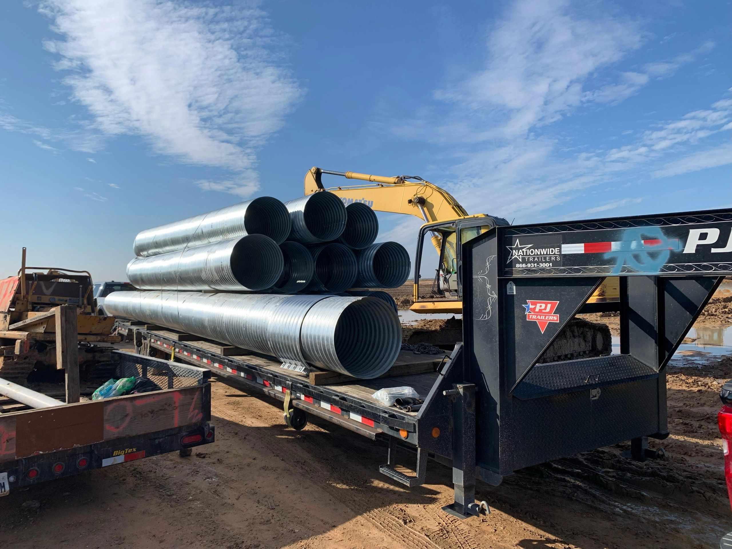 Excavator loading pipes onto flatbed at construction site