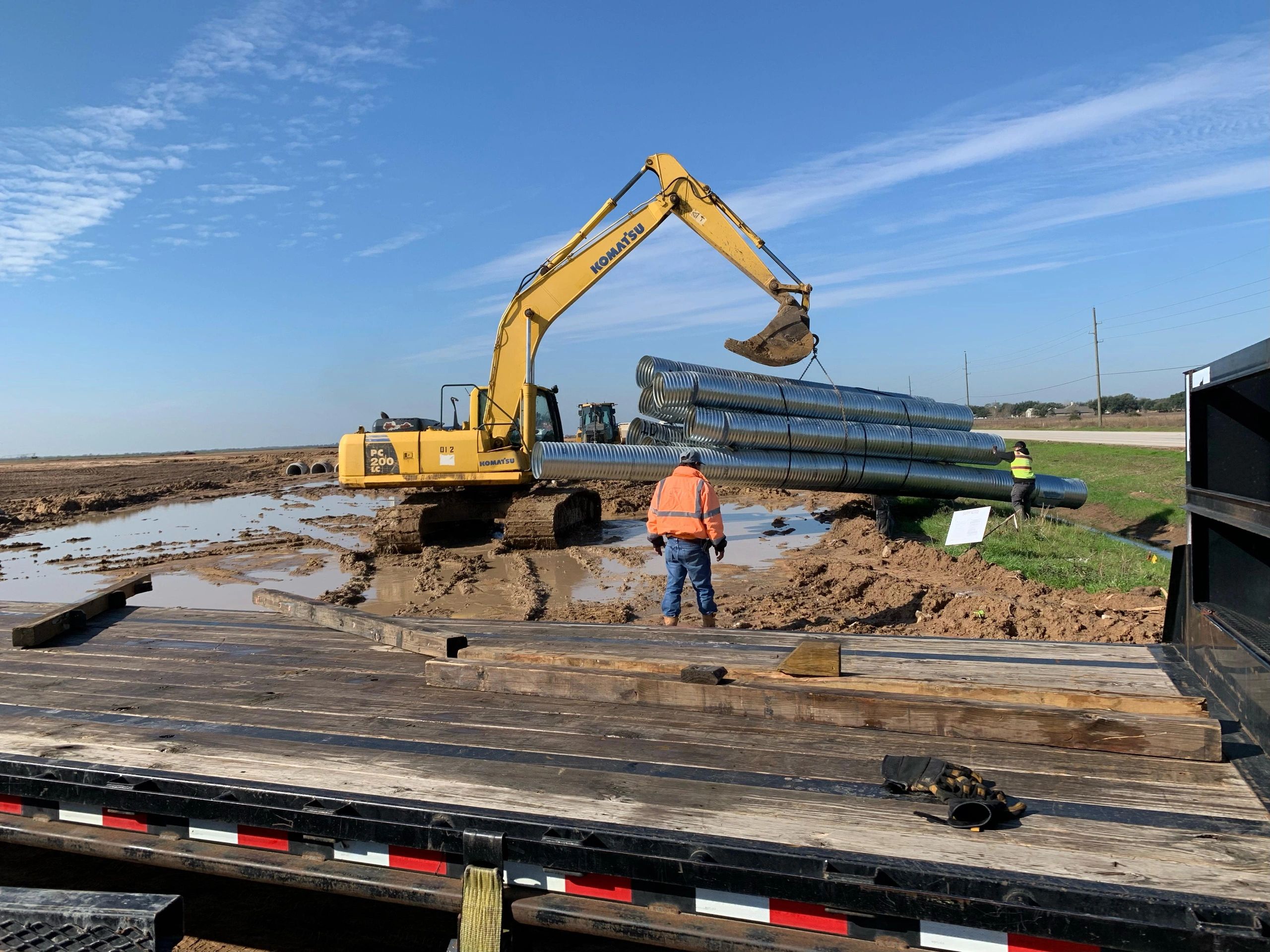 Excavator loading pipes flatbed trailer construction site